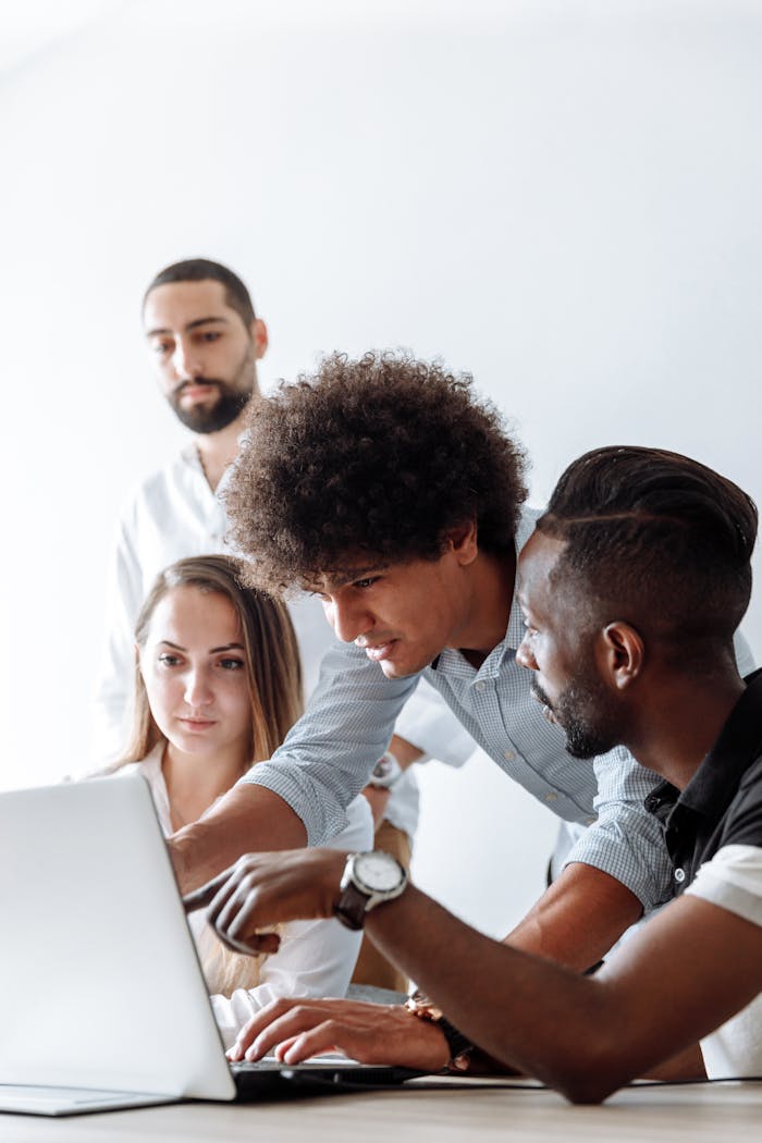 Group of professionals engaging in a collaborative discussion around a laptop in a modern office setting.